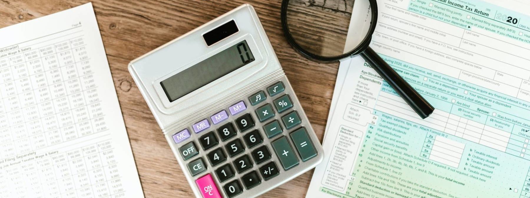 gray calculator and black magnifying glass on brown wooden surface