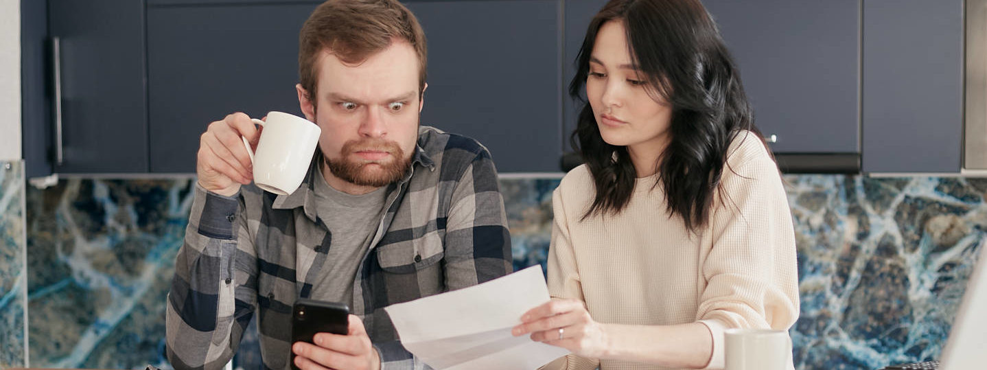 A man looking at the paper while holding a coffee and phone