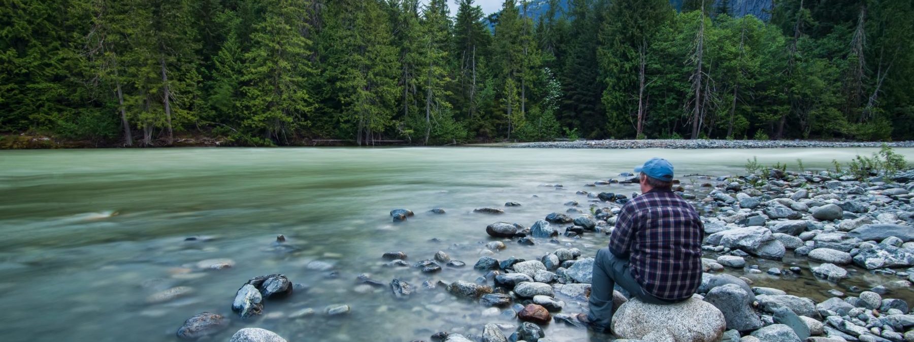 Person sitting on stone near body of water